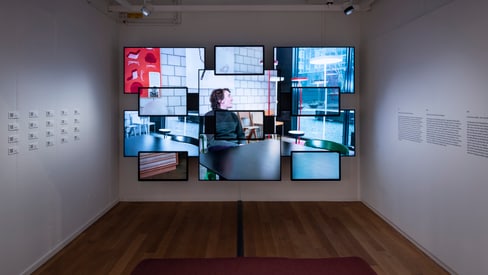 Kunstinstallation mit mehreren Bildschirmen an einer Wand in einem Raum.