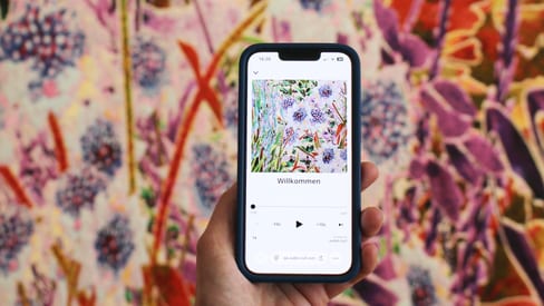 Hand hält Smartphone vor bunter Blumenwand.