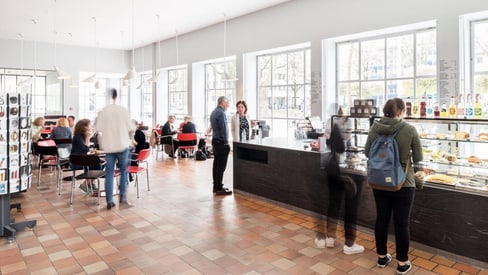 Menschen in einem Café mit Getränken und Gebäck in der Vitrine.