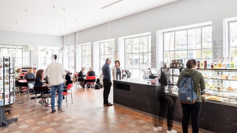 Menschen in einem Café mit Getränken und Gebäck in der Vitrine.