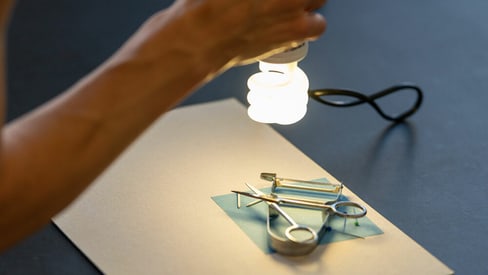 Hand hält Lampe über Solarpapier belegt mit Alltagsgegenständen.