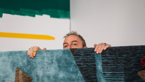 Eine Person, die hinter einem bunten Teppich hervorschaut.