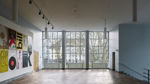 Lichtdurchflutetes Foyer mit Fenstern und an der Wand hängenden Plakaten.