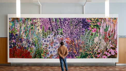 Person betrachtet ein grosses, buntes Gemälde von Blumen.