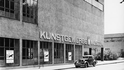 Schwarzweiss-Foto eines Kunstgewerbemuseums mit geparktem Auto.