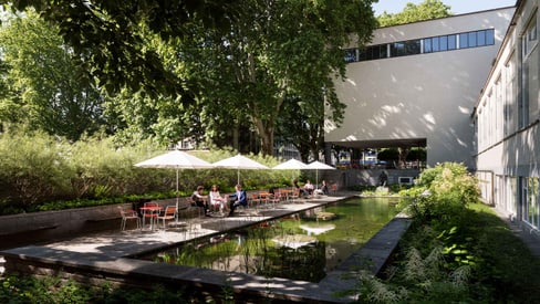 Garten mit Teich und Sitzbereich neben modernem Gebäude.