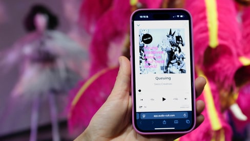 Hand hält Smartphone mit Musik-App vor leuchtend rosa Kostüm.