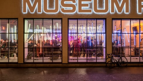 Nachtansicht eines Museums mit beleuchteten Fenstern und einem Fahrrad davor.