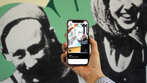 Hand hält Smartphone vor Schwarzweiss-Wandbild.