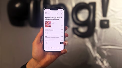 Hand hält Smartphone vor unscharfem Logo an der Wand.