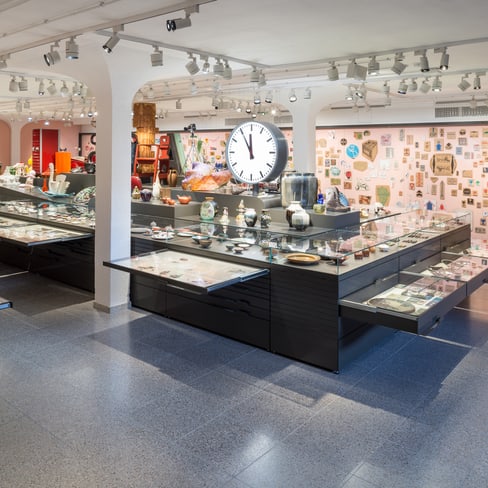 Innenraum eines Museums mit Ausstellungsvitrinen und Wanduhr.