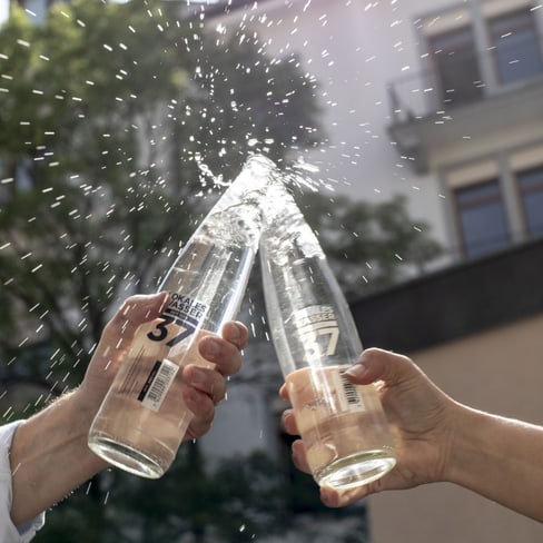 Zwei Wasserflaschen stossen an, Wasser spritzt heraus."  