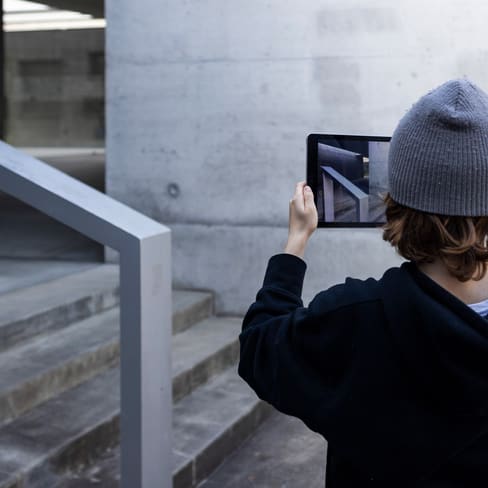 Person mit grauer Mütze macht Foto mit Tablet von Treppe.