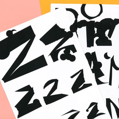 Abstrakte schwarze Buchstaben auf weissem Papier vor rosa Hintergrund.