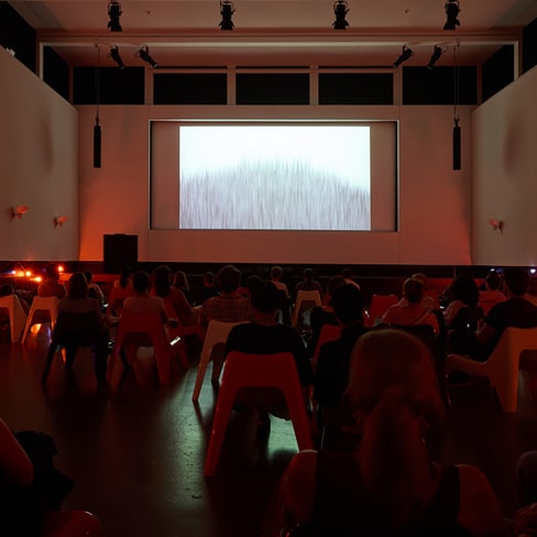 Menschen sehen in einem dunklen Raum einen Film auf einer Leinwand an.