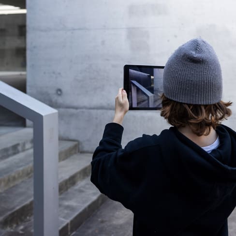 Person mit Mütze fotografiert Treppe mit Tablet.