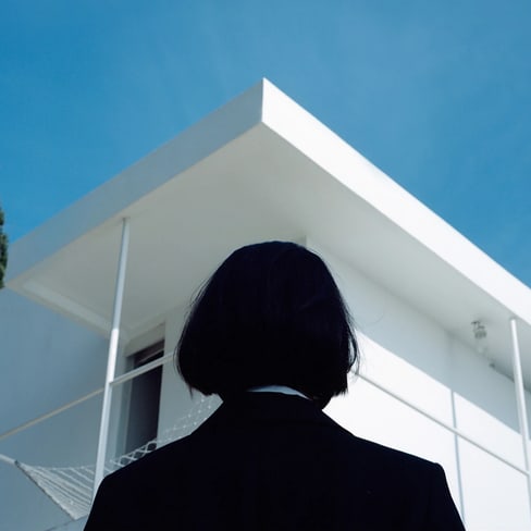 Person steht vor modernem, weissem Gebäude mit blauem Himmel.