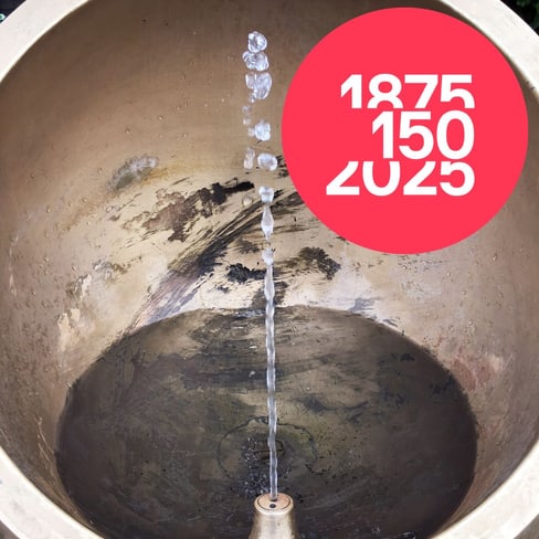 Wasserstrahl in Brunnen mit rotem 150-Jahre-Logo.",