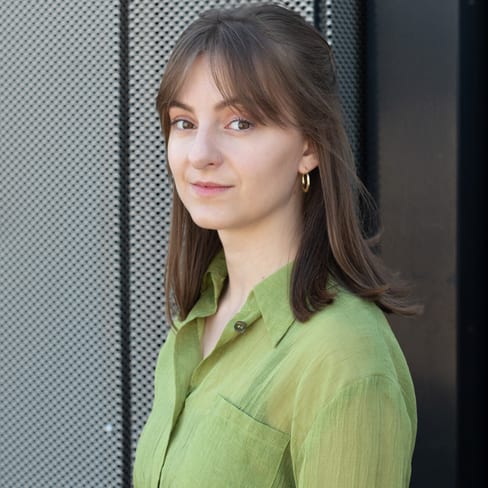 Frau in grünem Hemd vor Metallwand stehend.