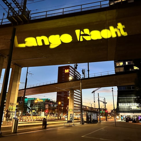 Gelbes Lichtprojektionsschild 'Lange Nacht' auf Brücke bei Nacht.