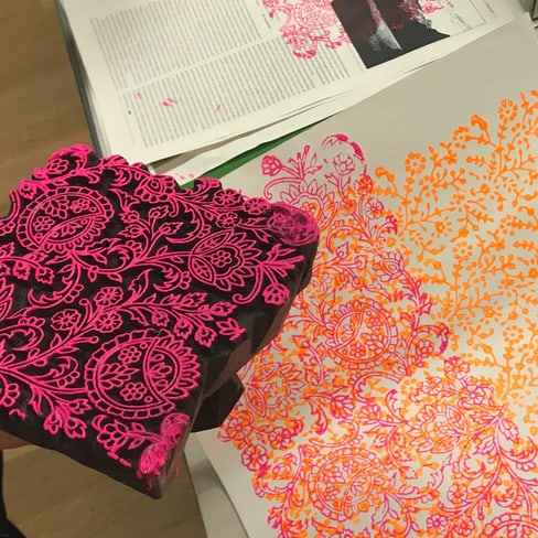 Holzblock mit floralem Muster neben bedrucktem Papier in Pink und Orange.",