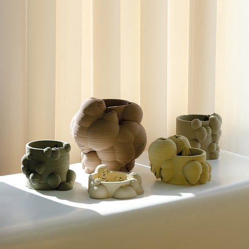 Mehrere organisch geformte Keramiktöpfe auf Fensterbank vor Jalousien.