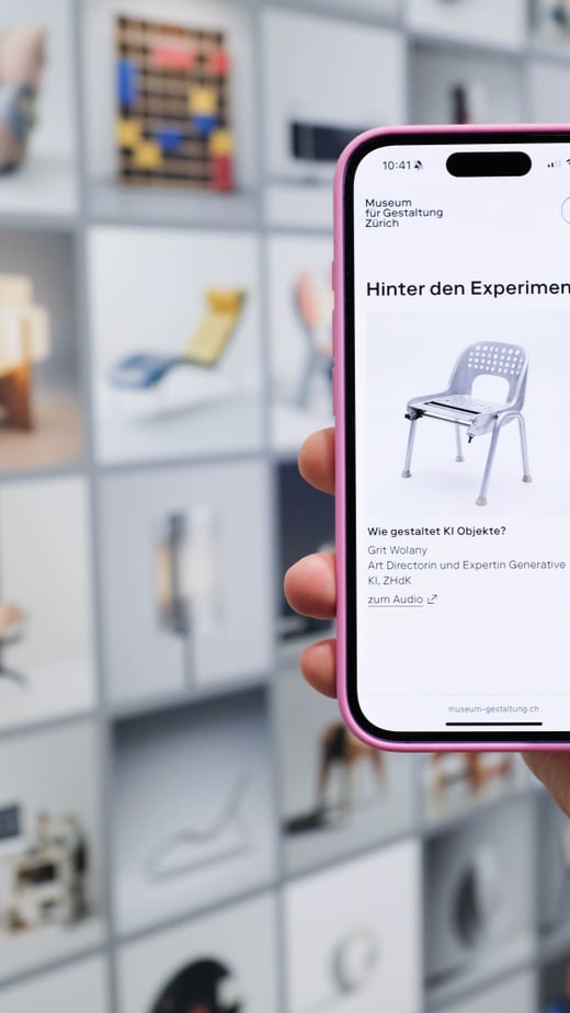 Hand hält Smartphone vor Wand mit Bildern, zeigt Stuhlbild auf Bildschirm.