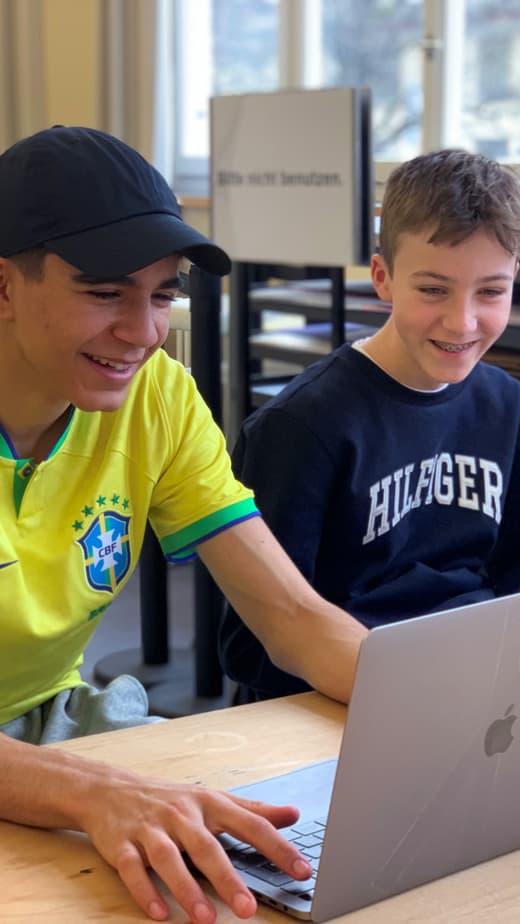 Zwei Jungen lachen und schauen auf einen Laptop Bildschirm.