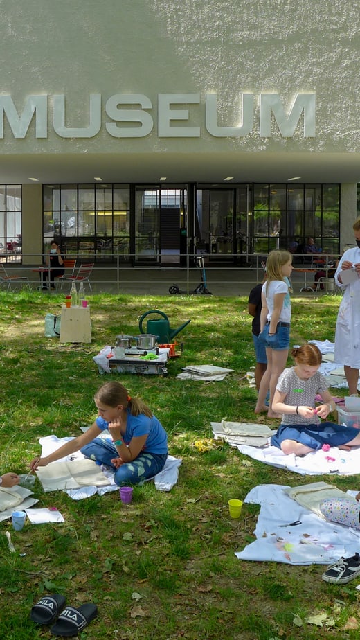 Kinder Drucken auf Rasen vor Museumseingang.