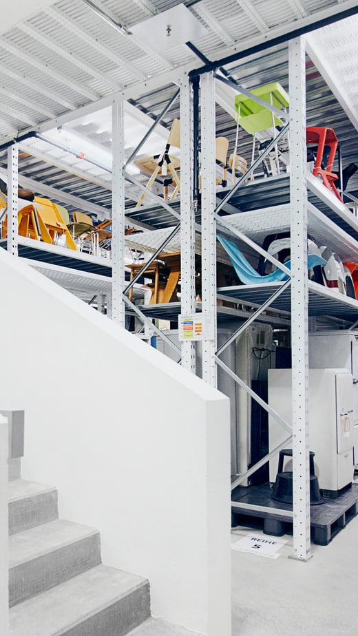 Weisse Treppe neben Regalen voller bunter Stühle in einem Lager.