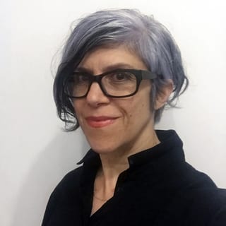 Lächelnde Person mit Brille und kurzem, grauem Haar vor weissem Hintergrund.