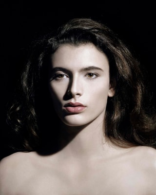 Porträt einer Person mit langen Haaren vor dunklem Hintergrund.