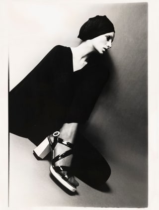 Schwarz-weiss Porträt einer sitzenden Person mit hohen Schuhen und Turban.