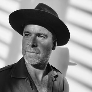 Porträt eines Mannes mit Hut, Schattenmuster im Hintergrund.