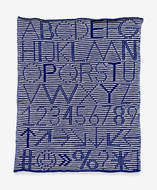 Gewebte Decke mit blauem Alphabet und Zahlen auf weissem Hintergrund.