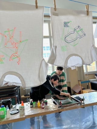 Personen beim Siebdruck mit aufgehängten Tüchern im Vordergrund.