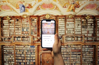 Hand hält ein Smartphone vor einer hohen Bücherwand.
