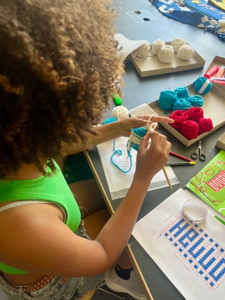 Person strickt mit buntem Garn und Stricknadeln am Tisch sitzend.