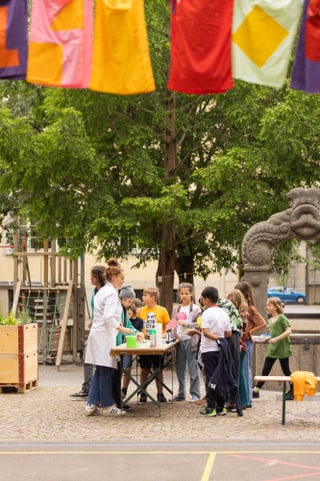 Kinder im Freien mit einem Siebdruckstand unter bunten Fahnen.