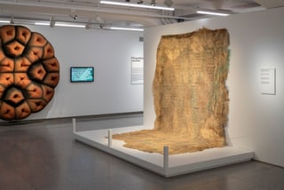 Kunstinstallation mit Wandteppich und abstrakter Skulptur in Galerie.