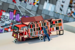 Buntes Papiermodell eines Lastwagens mit Regalen und Figur davor.