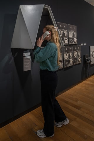 Person telefoniert in einer Ausstellung mit alter Telefonzelle.