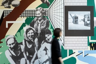 Frau geht an Wandbild mit historischen Fotos vorbei.