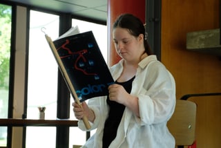 Frau sitzt und liest ein Buch drinnen.