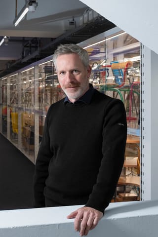 Mann in schwarzem Pullover in modernem Raum mit Glaswand.