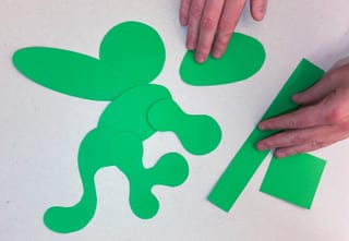 Grüne Papierformen und Hände auf weissem Hintergrund.