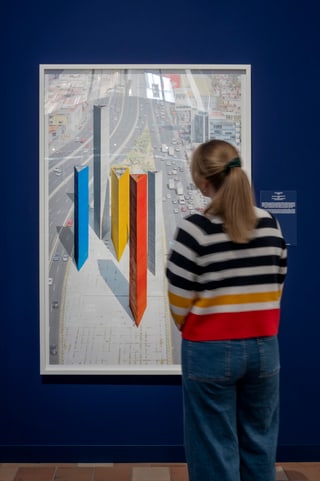 Person betrachtet Kunstwerk mit Stadtbild und bunten Formelementen.