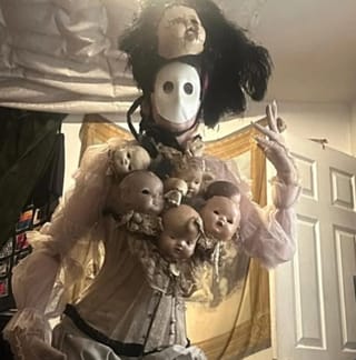 Outfit mit Puppenköpfen und einer weissen Maske.