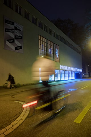 Nachtaufnahme eines Radfahrers vor einem beleuchteten Museum in Zürich.