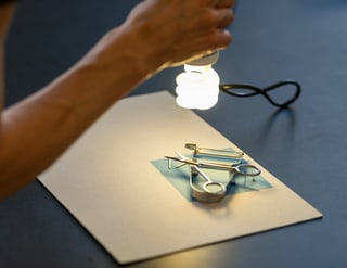 Hand hält Lampe über Solarpapier belegt mit Alltagsgegenständen.